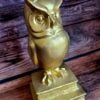 Statuetka-złota sowa stojąca na stosie książek
